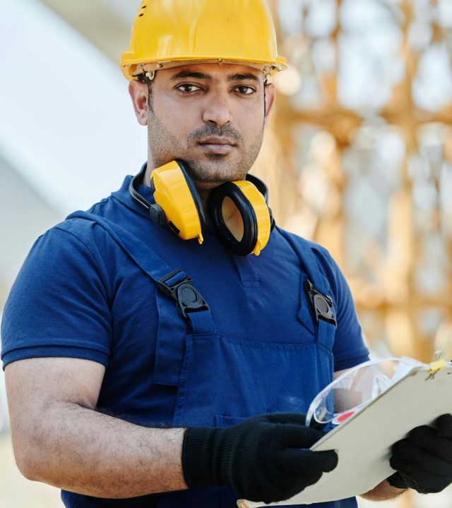 pexels photo 8960992 8960992 Focused construction worker outdoors wearing safety gear, holding a clipboard at a building site.
